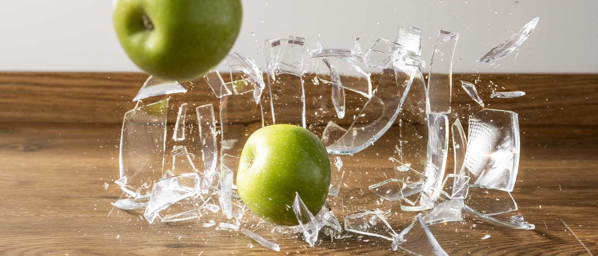 en glassvase med epler faller ned på et brunt vinylgulv og knuser